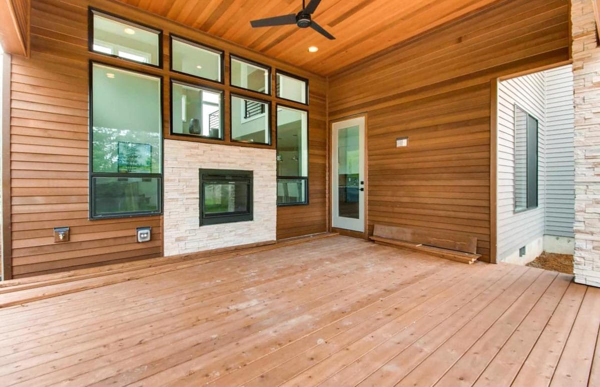 Covered outdoor living space with wood siding, stone fireplace, and large windows.