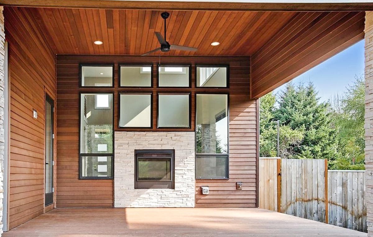 Modern house exterior with wood siding, stone fireplace, and large windows.