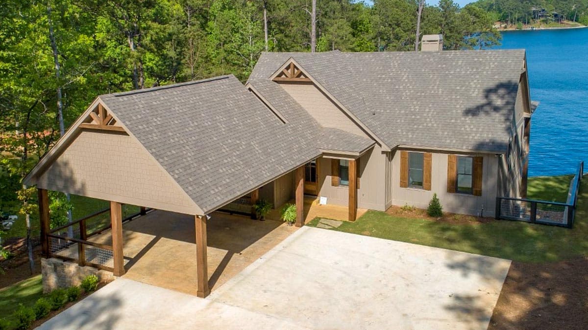 House plan exterior featuring a covered carport with exposed rafters, gable accents, and wood shutters, set by a lake.