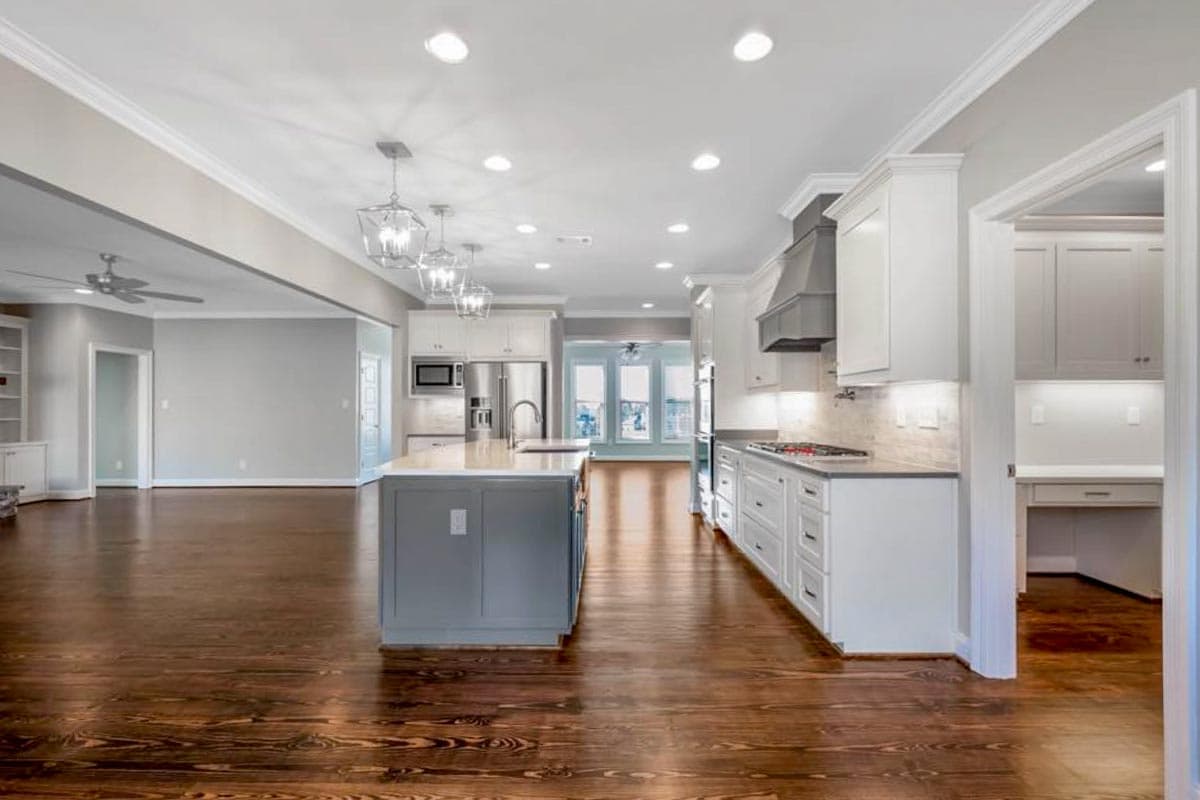 Interior view of a spacious kitchen with a large island, stainless steel appliances, and an open view to a living area.