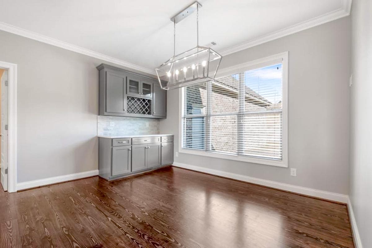 Dining area with gray built-in cabinetry featuring a wine rack, a large window, and a modern chandelier.