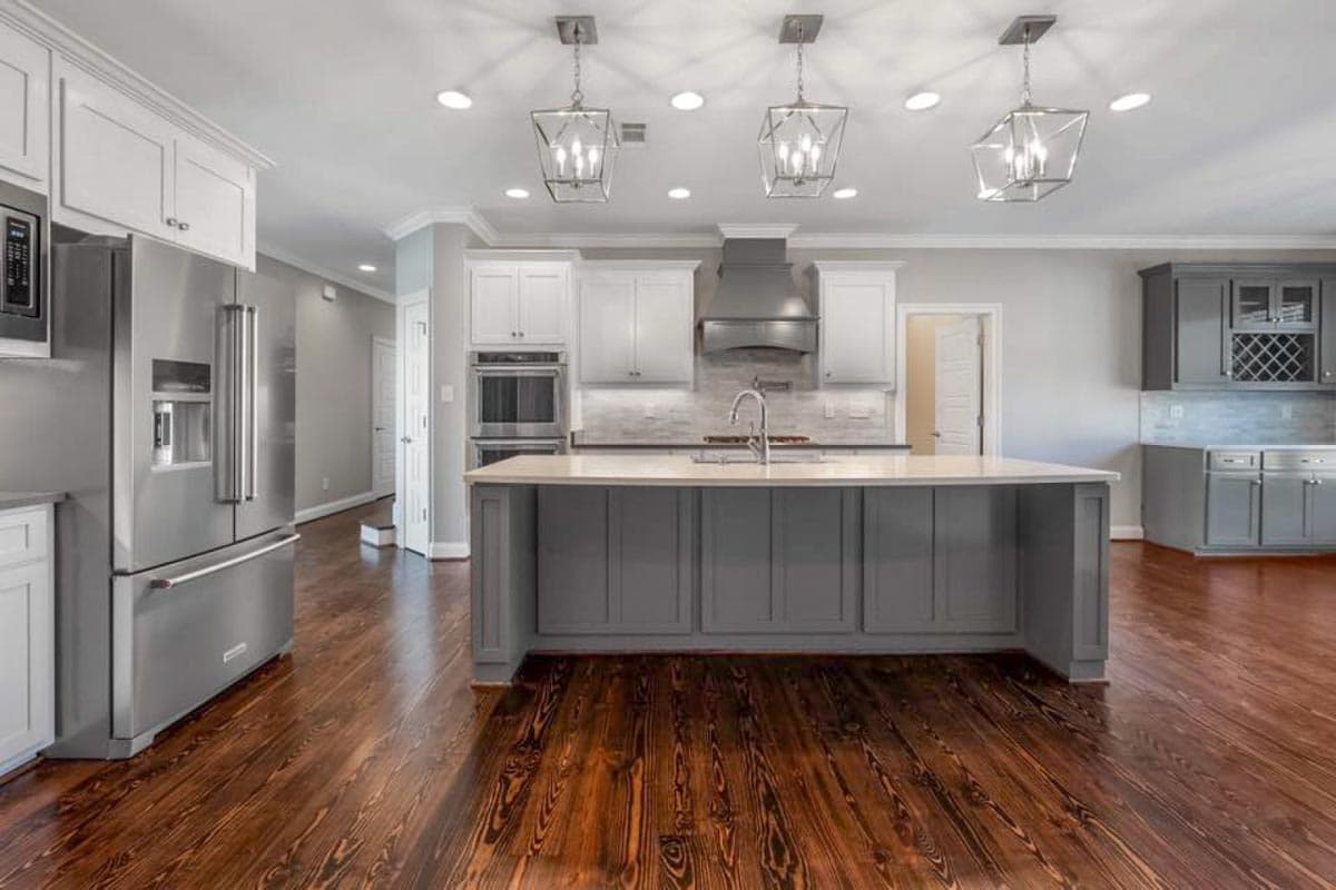 Kitchen with gray island, stainless steel appliances, white cabinets, and pendant lighting.