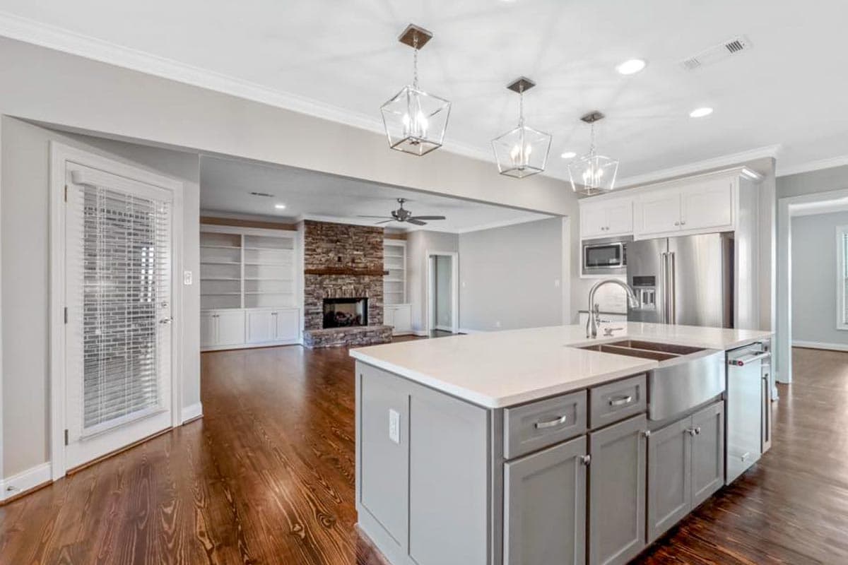 Kitchen with island and farmhouse sink open to living area with stone fireplace and built-in shelving.