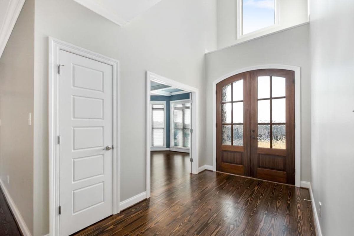 Interior view of foyer with vaulted ceiling, double glass doors, and paneled interior door.