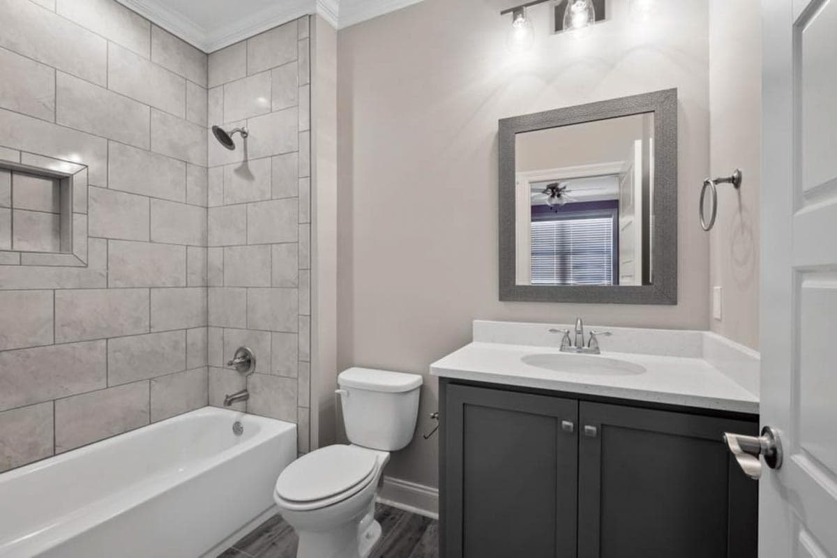 Bathroom with a tub-shower combo, gray tile surround, vanity with dark cabinets, and white countertop.