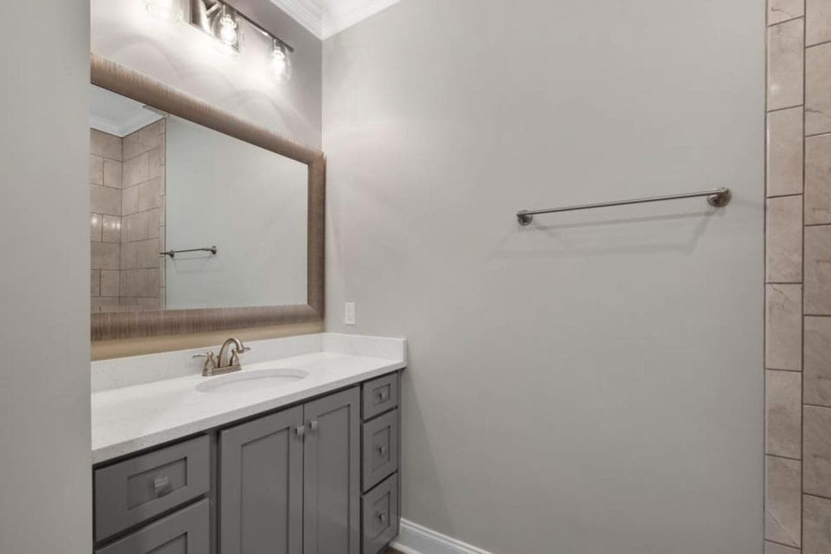 Bathroom with gray vanity, white quartz countertop, large framed mirror, and tiled shower wall.