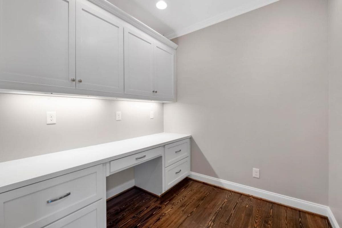 Built-in white cabinetry with integrated desk and drawers, under-cabinet lighting, and dark wood floors.