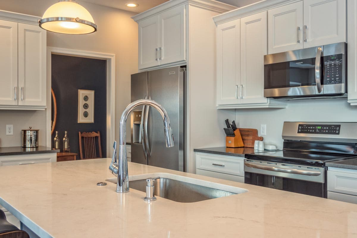 Kitchen with white cabinets, stainless steel appliances, island sink with chrome faucet, and a doorway to another room.