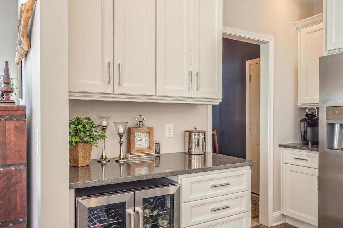 Kitchen wet bar with white cabinetry, dual wine fridges, and granite countertop. Doorway reveals hallway.