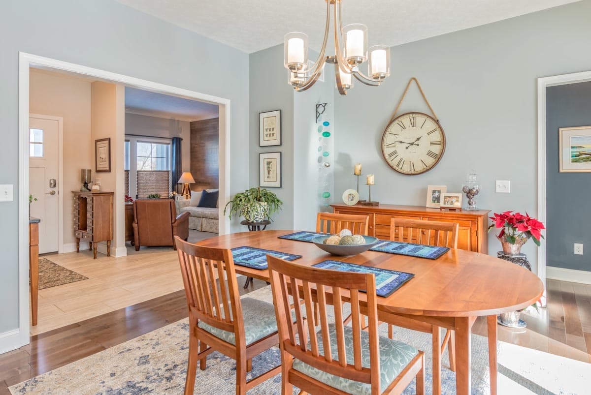 Dining room with oval wood table, chairs, buffet, large wall clock, and view into living room and entryway.