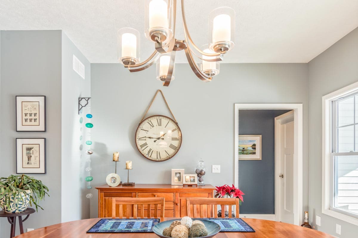 Dining room with wooden table, chairs, buffet, chandelier, and large wall clock.