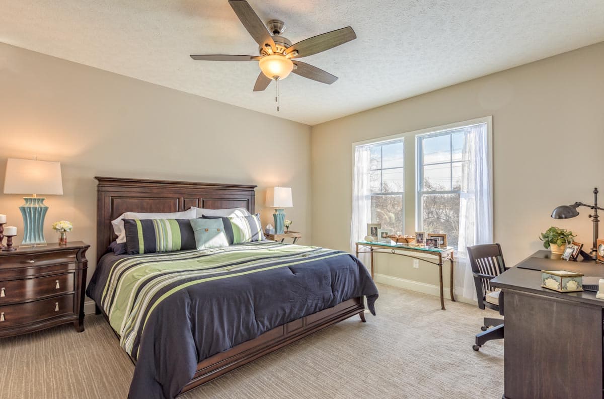 Bedroom with a dark wood bed, striped bedding, nightstands, and a desk with a chair next to two windows.