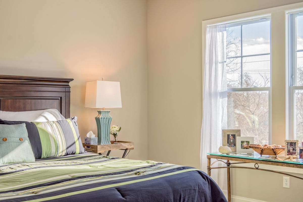 Bedroom with dark wood headboard, striped bedding, and large windows with sheer curtains.