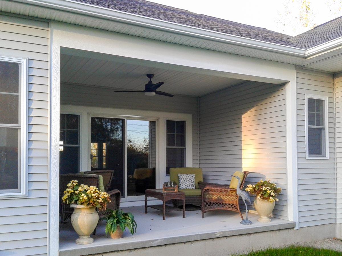 House plan exterior featuring a covered porch with seating, sliding glass doors, and vinyl siding.