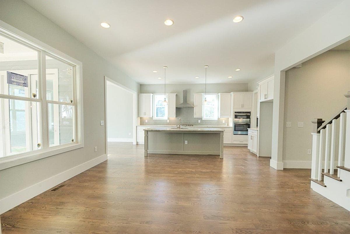 Open concept kitchen with large island, white cabinetry, double ovens, and island pendant lighting. Stairs visible to the right.