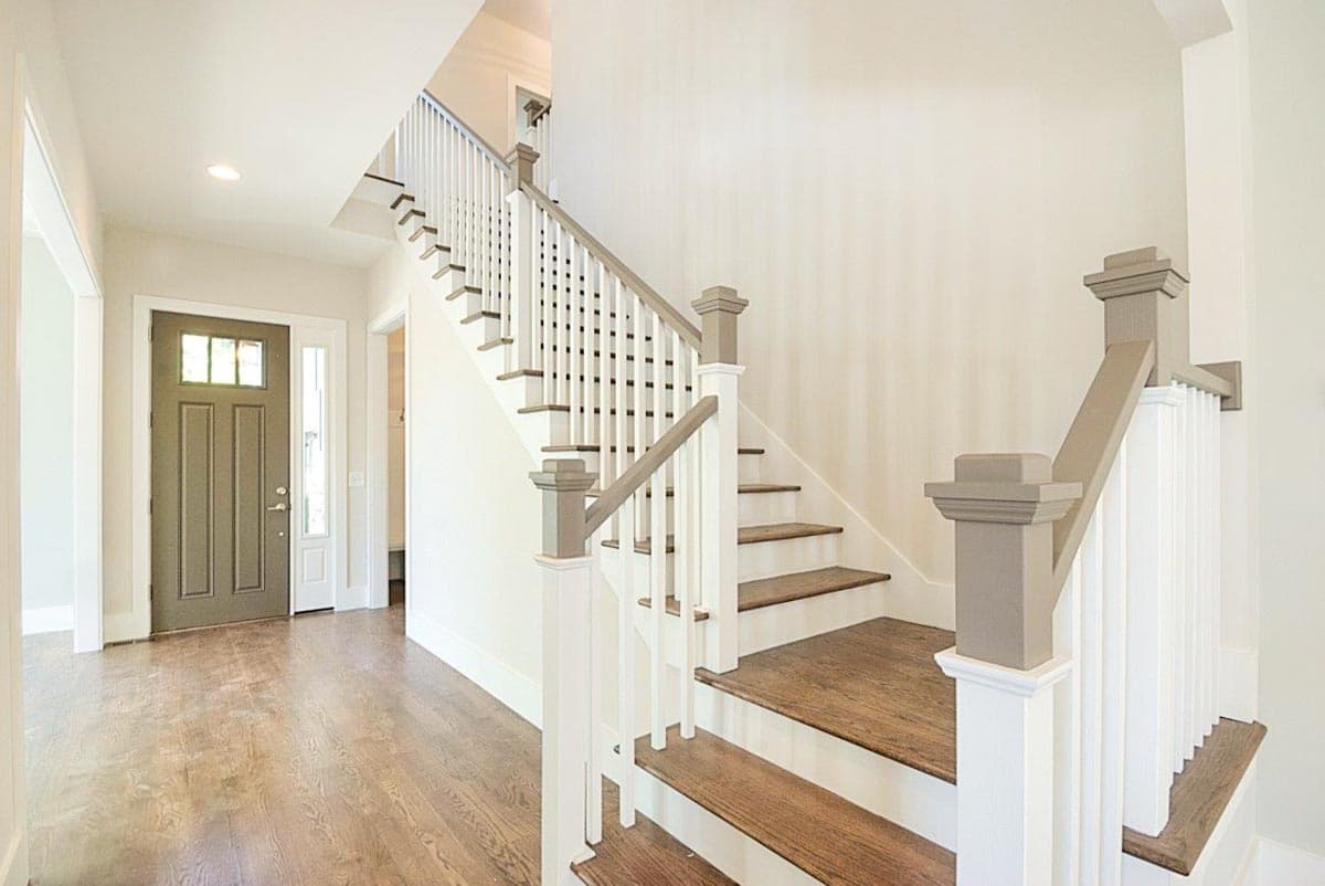 Interior view of a house entryway with a staircase featuring wood treads and a white balustrade.