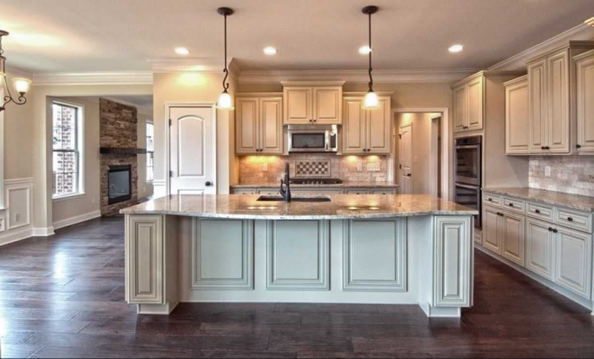 Interior view of a kitchen with a large island, granite countertops, and a stone fireplace visible in an adjacent room.