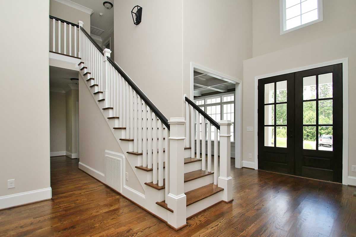 Interior view of a foyer with a staircase featuring white balusters, dark handrails, and wood treads, plus double glass doors.