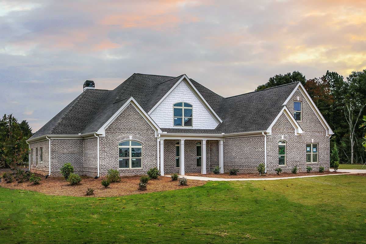 House plan exterior: Brick one-story home with a covered front porch, arched windows, and gabled dormer.