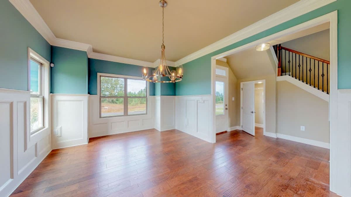 Interior view of dining area with wainscoting, large windows, chandelier, and staircase.