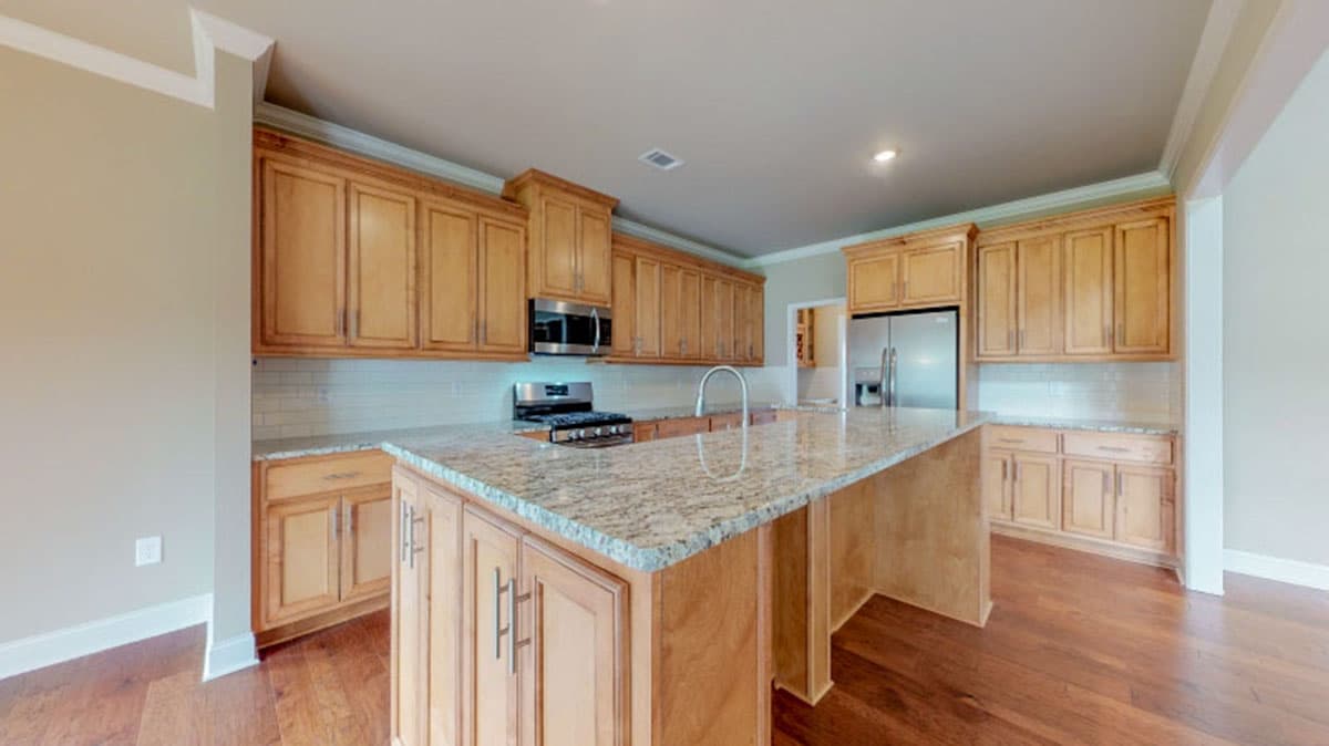 Kitchen with light wood cabinets, granite island with sink, stainless steel appliances, and subway tile backsplash.