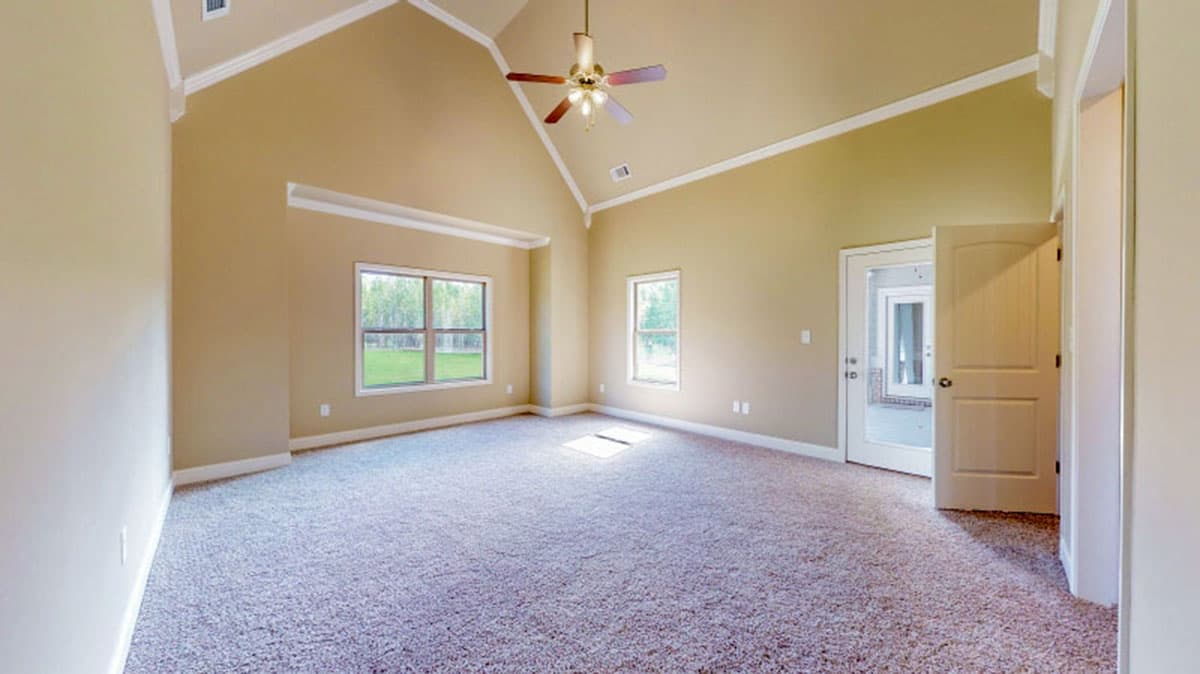 Interior view of a bedroom with vaulted ceiling, ceiling fan, two windows, and a doorway leading to another room.