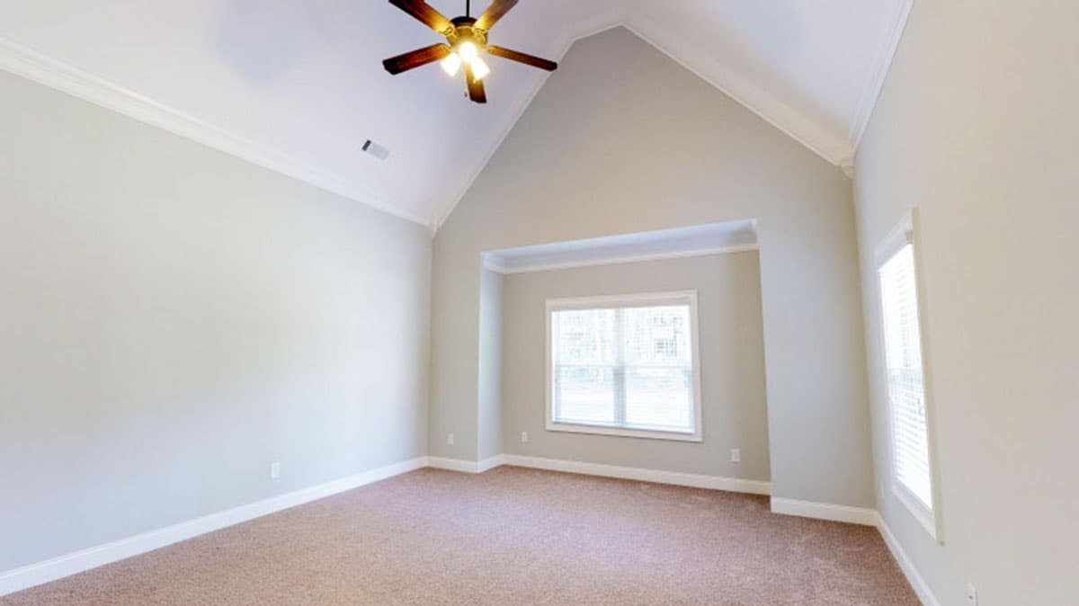 Empty room with vaulted ceiling, fan, and windows.