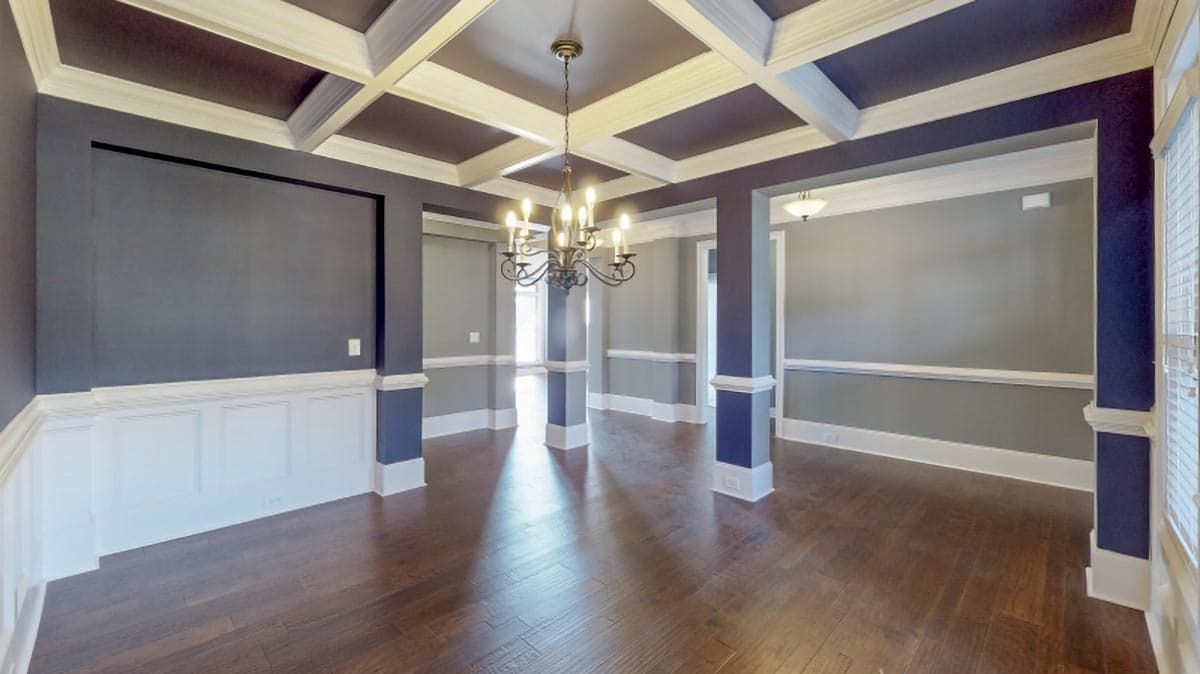 Dining room with coffered ceiling, wainscoting, columns, and chandelier.