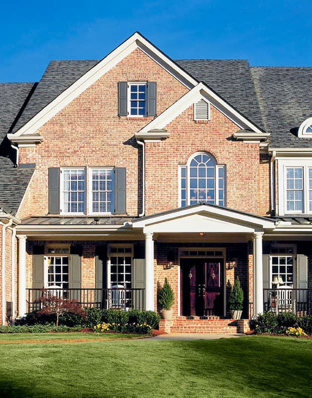 House plan exterior: brick two-story home with covered porch, central gable, dormer window, and arched entryway.