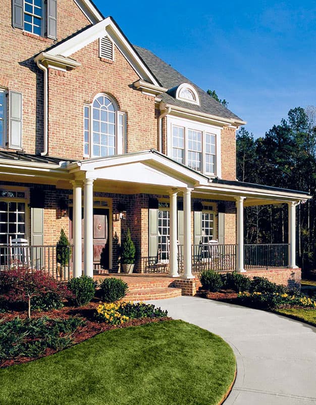House plan exterior: Traditional brick two-story home with a wrap-around porch, arched windows, and dormers.
