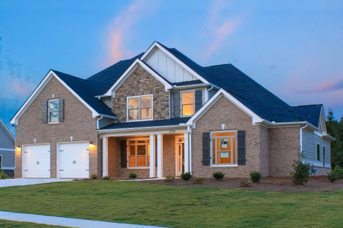 Two-story house plan exterior with a brick facade, prominent gables, a covered front porch, and a side-entry two-car garage.