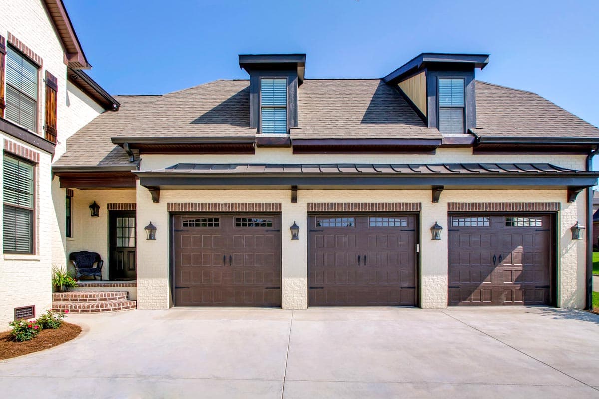 House plan exterior with three-car garage, brick accents, dormers, and covered entryway.