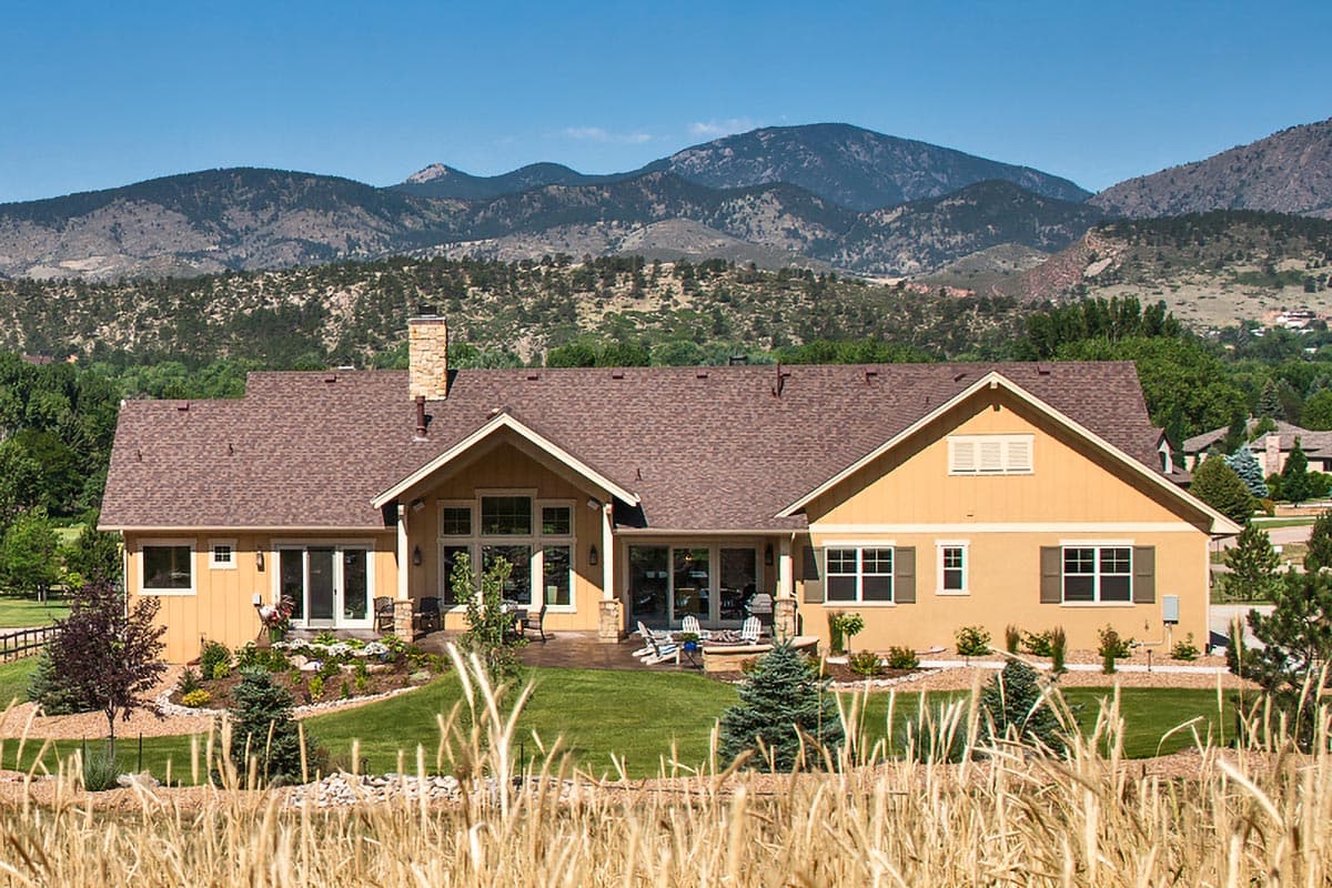 House plan exterior of a one-story home with a prominent gable, stone chimney, and large rear-facing windows.