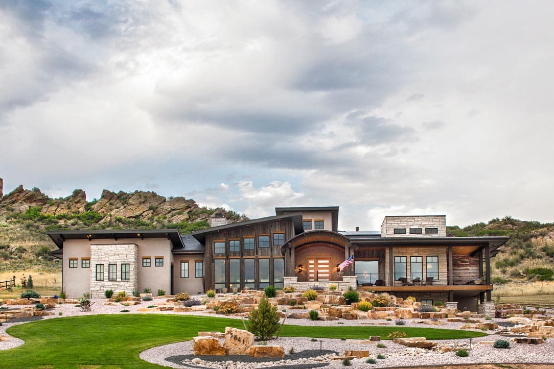 Modern house plan exterior with stone and wood facade, multiple gables, and large windows. Two stories are evident.