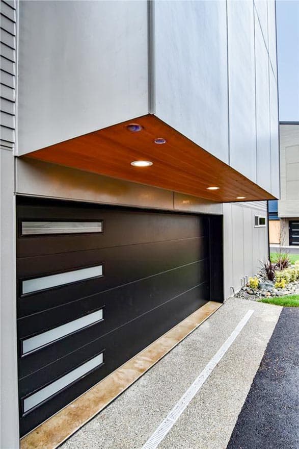 Modern house exterior with black segmented garage door, wood soffit, and exterior lighting.