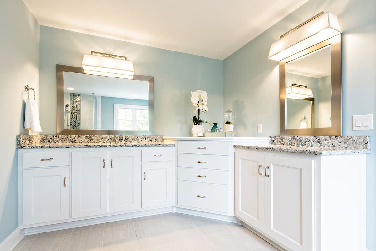 Bathroom vanity with white cabinets, granite countertops, dual sinks, and modern lighting.