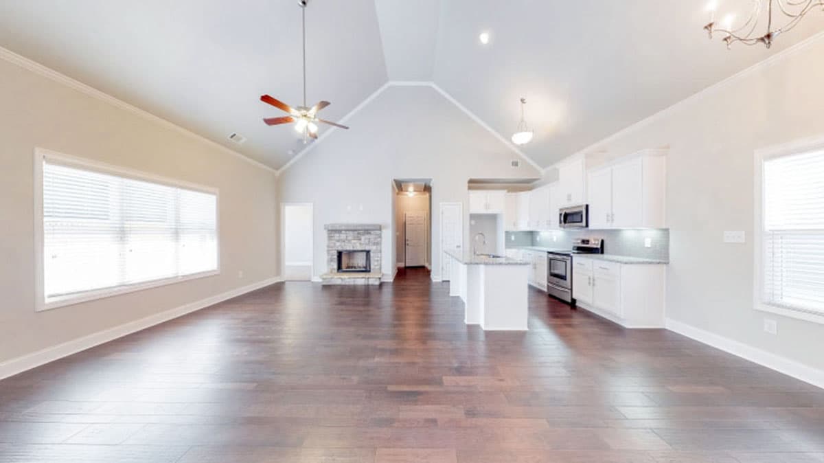 Open concept living area and kitchen with vaulted ceiling, stone fireplace, island, and white cabinetry.