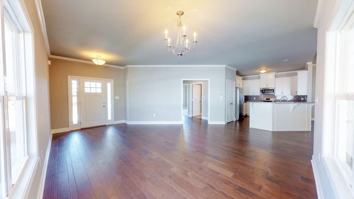 Interior view showing an open-concept living area with entryway, kitchen with island, and hardwood floors.