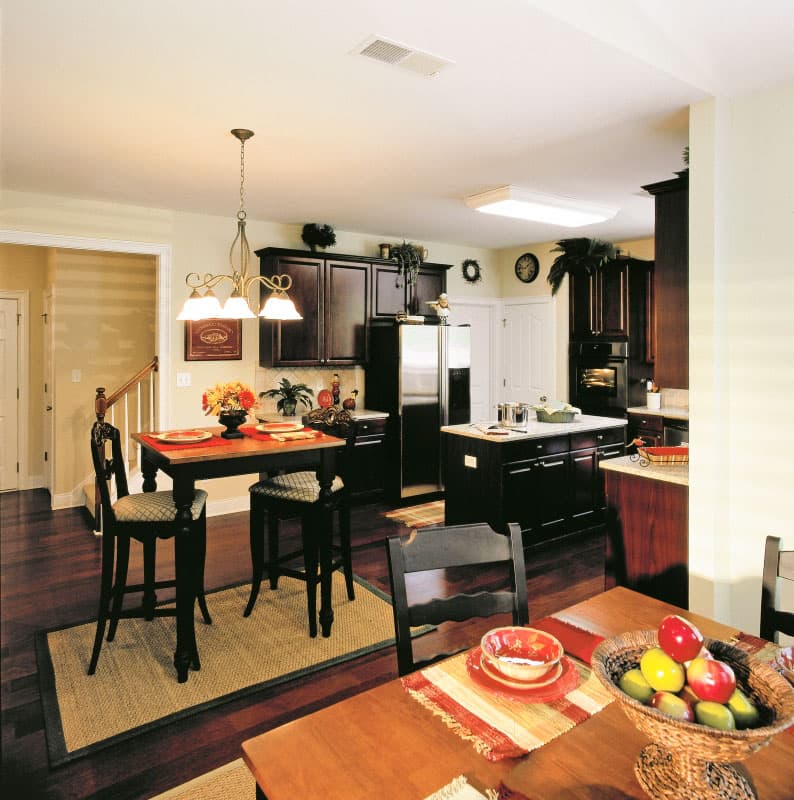 Kitchen with dark wood cabinets, stainless steel refrigerator, island, and two dining areas.
