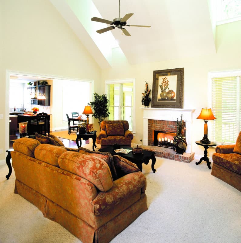 Living room with vaulted ceiling, brick fireplace, and open access to kitchen and dining areas.