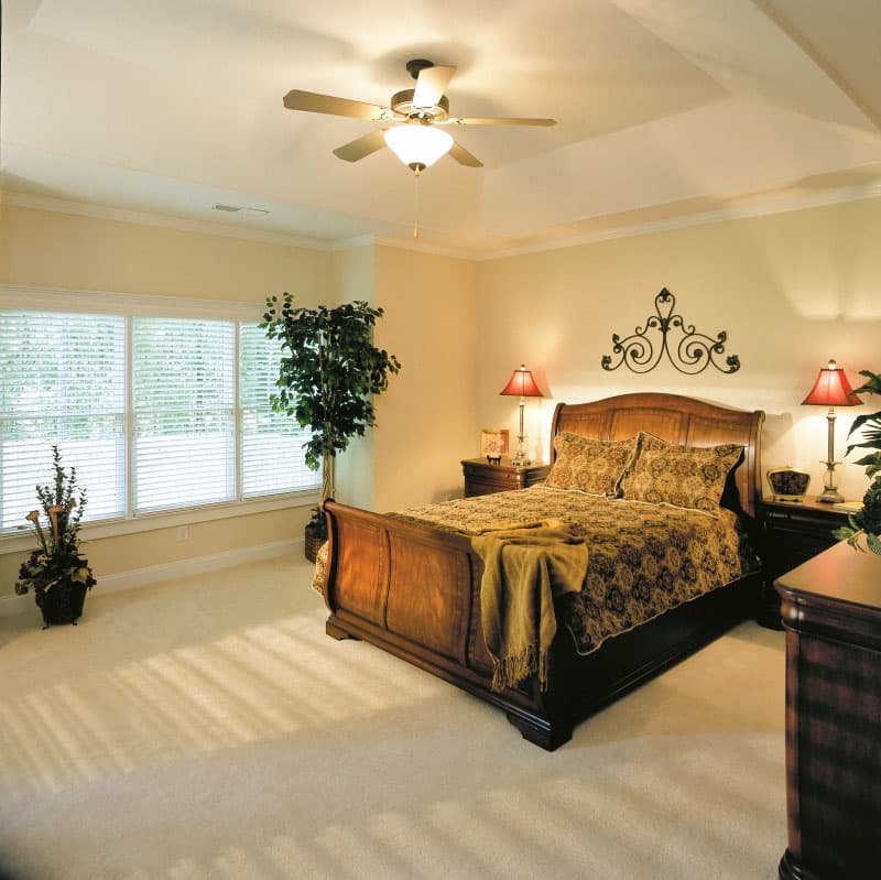 Bedroom with tray ceiling, ceiling fan, and large windows. Includes a wooden bed, nightstands, and decorative wall art.