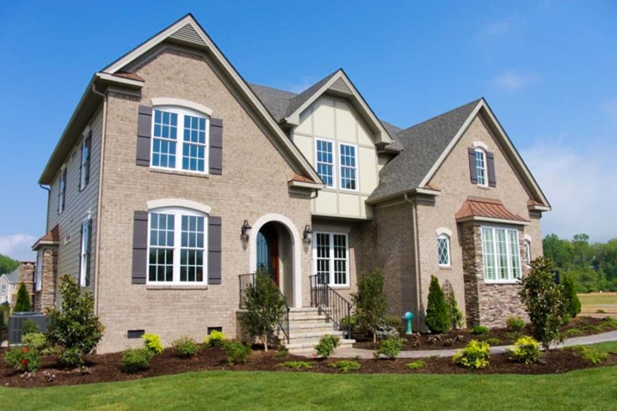 House plan exterior. Two-story brick home with gabled roof, dormers, and front entry porch with steps and railing.