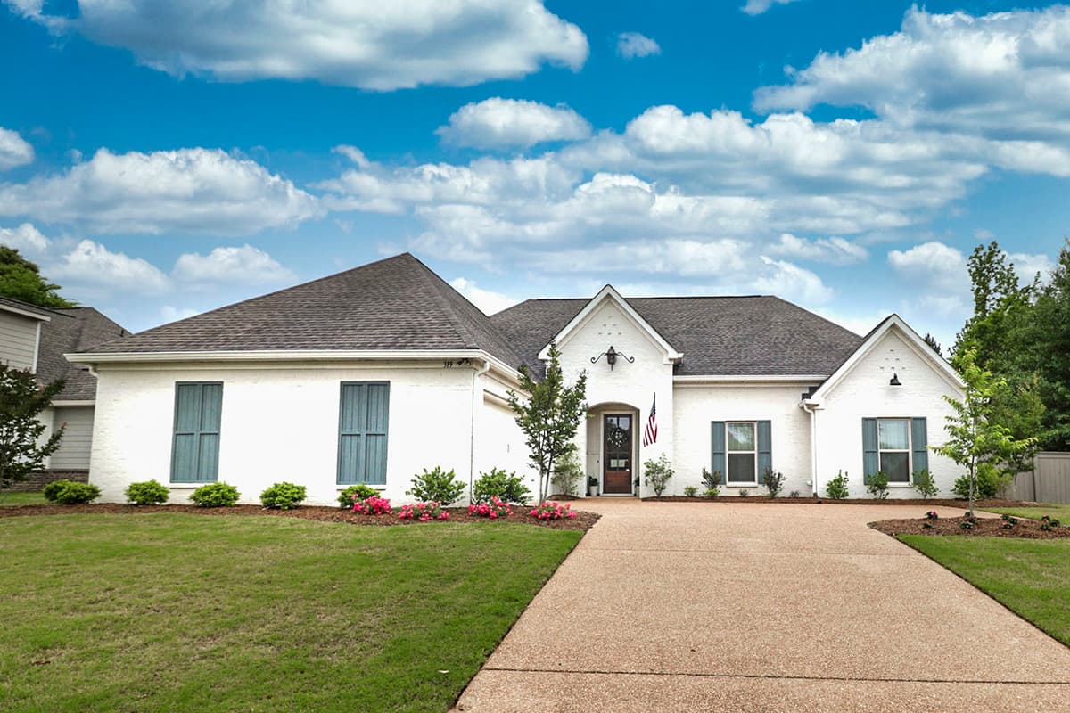 House plan exterior: single-story white brick home with a mix of gables, arched entry, and three-section windows.