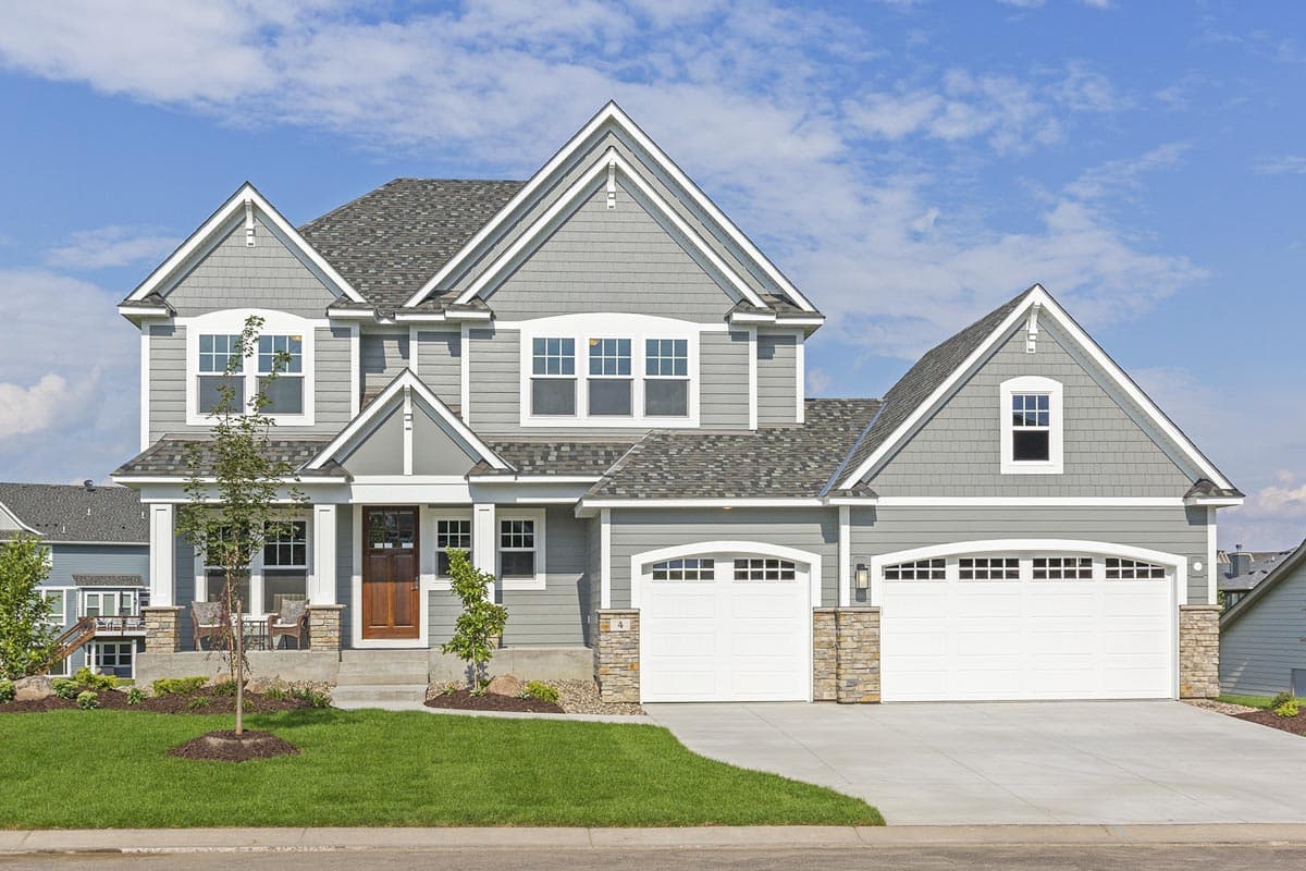 House plan exterior: Two-story dwelling with shingle siding, gabled roof, covered porch, and attached three-car garage.