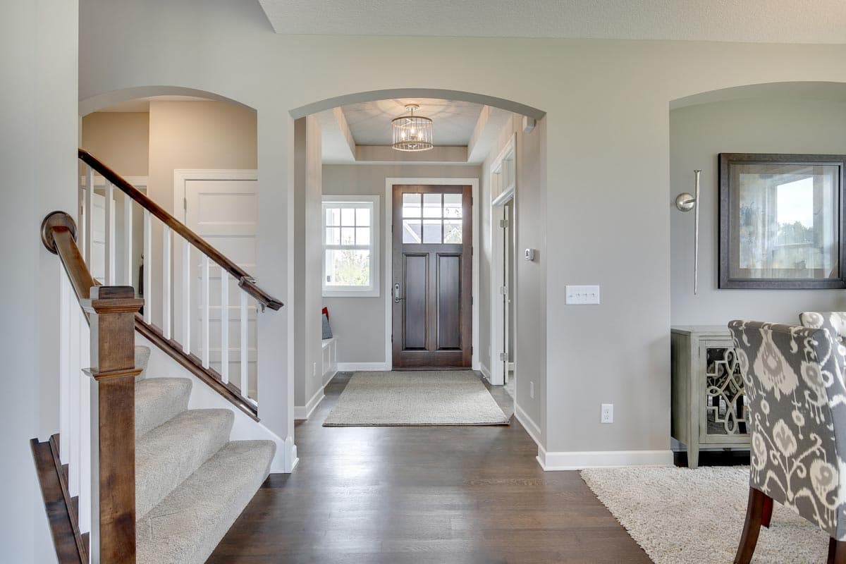 Interior view of a foyer with a wooden front door, a carpeted staircase, and an open layout.