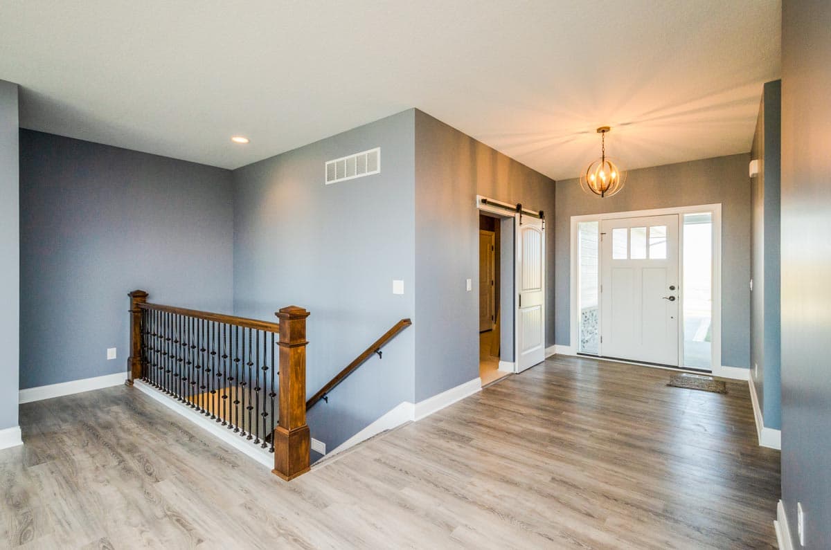 Interior view of a house entrance with a staircase, sliding barn door, and glass-paneled front door.