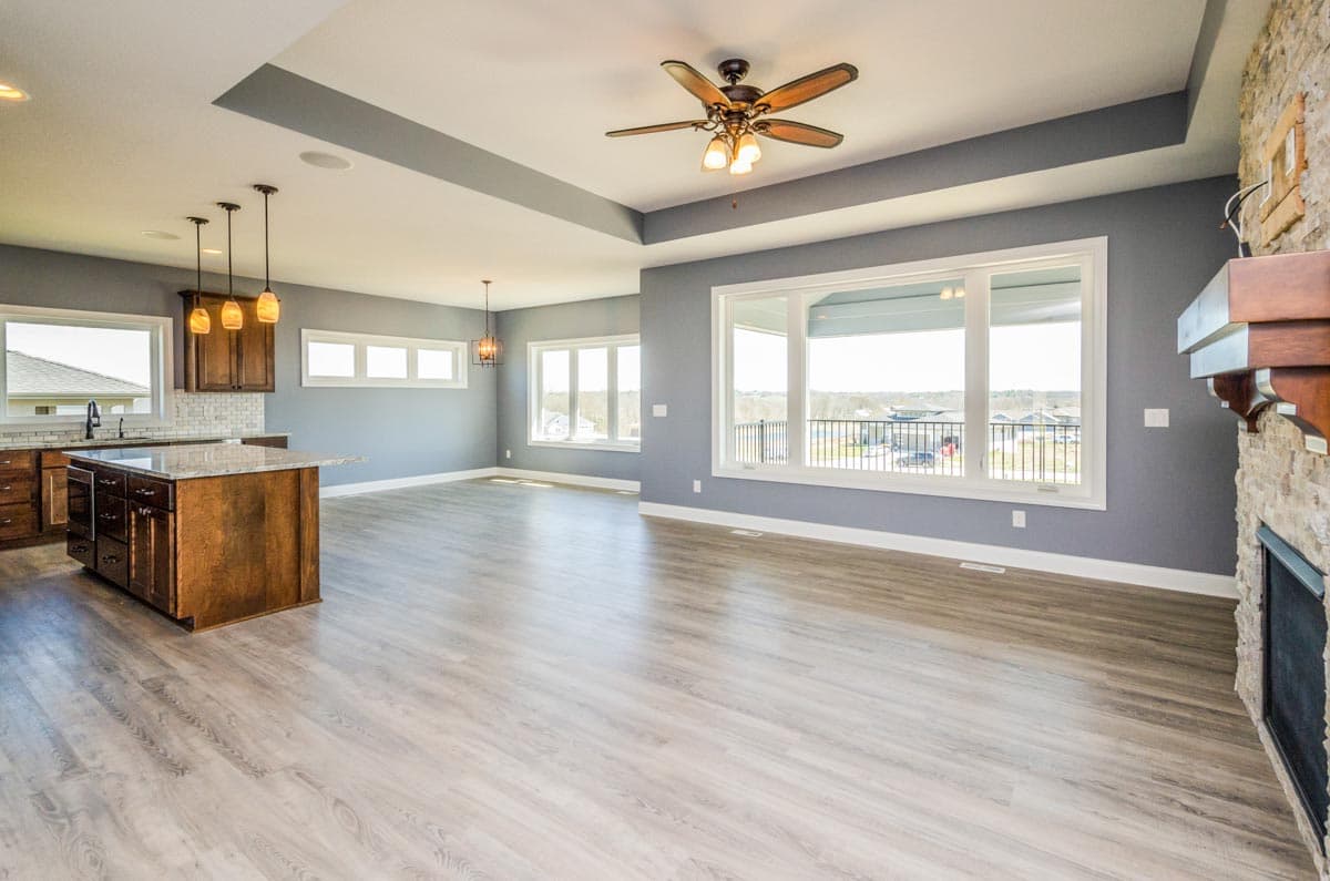 Open concept living area featuring a kitchen island, gas fireplace, tray ceiling, and large windows.
