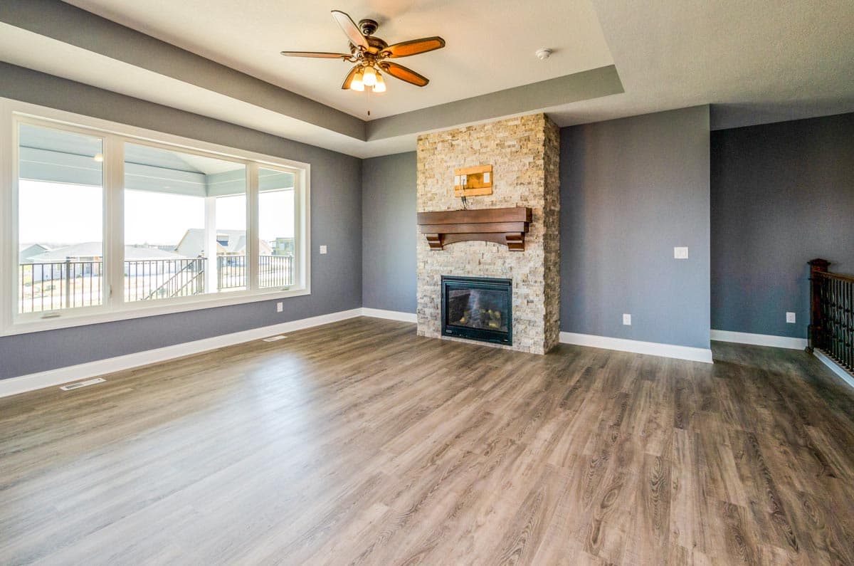 Great room with tray ceiling, stone fireplace, and large picture window with view of covered porch.