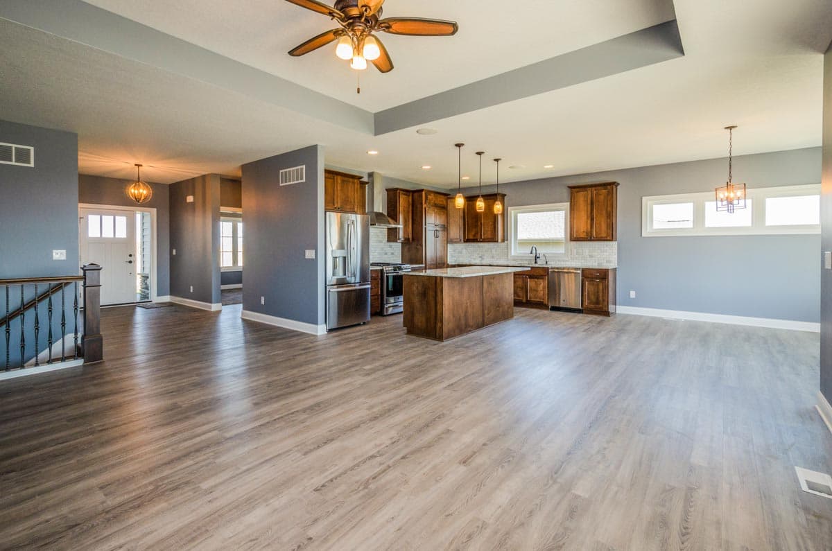 Open concept living and kitchen area with island, wood cabinetry, stainless steel appliances, and vaulted ceiling.