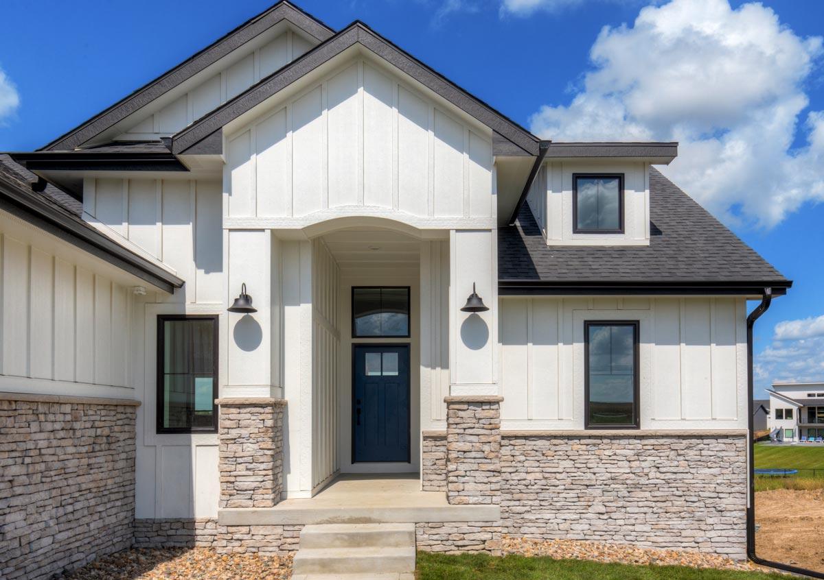 House plan exterior featuring white board-and-batten siding, stone accents, a dark blue door, and a dormer.